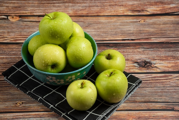 Fresh green apples with water drops on them in a blue bowl, top view