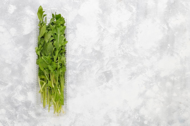 Free photo fresh green ruccola or arugula leaves in plastic boxes on grey concrete