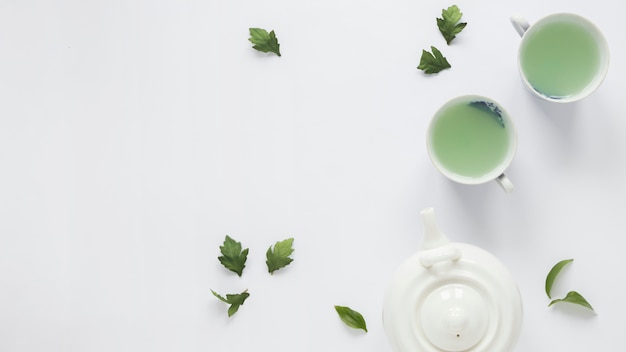 Fresh green tea with tea leaves and teapot on white background