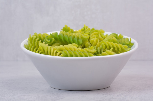 Fresh green uncooked spiral macaroni on white plate