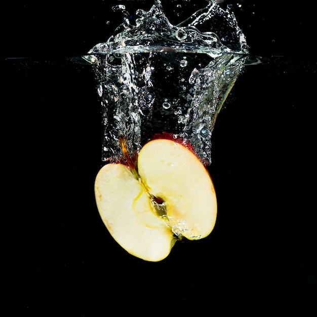 Fresh halved apple with water splash on black background