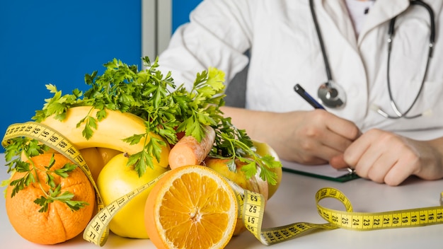 Fresh healthy fruits with measuring tape on dietician's desk