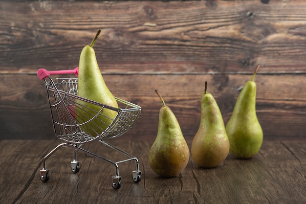 Free photo fresh juicy pear placed in small trolley on wooden background