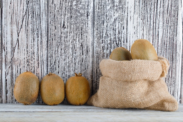 Free photo fresh kiwi in a sack on a wooden table. side view.