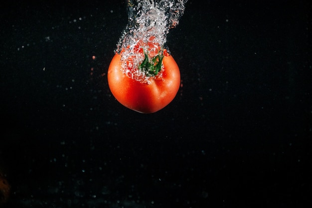 Fresh large tomato falls in water and makes bubbles