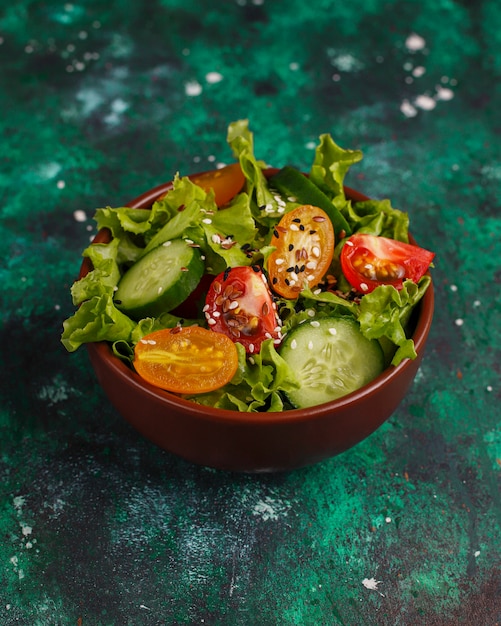 Free photo fresh lettuce salad with yellow tomatoes, slices,cherry tomatoes,seeds bowl on dark,