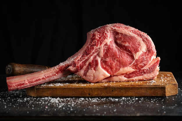 Fresh meat tomahawk steak on old wooden board. Dark background. Closeup