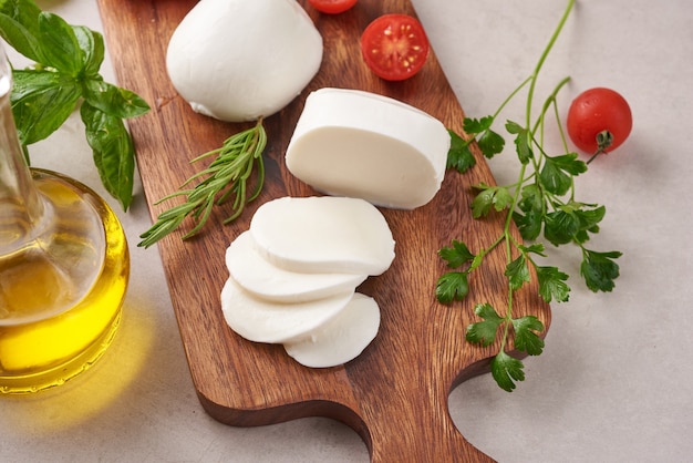 Fresh mozzarella cheese, Soft italian cheeses, tomato and basil, olives oil and rosemary on wooden serving board over light wooden surface. Healthy food. Top view. Flat lay.