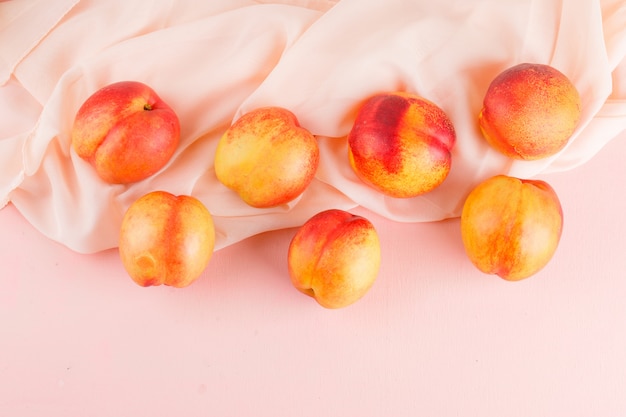 Fresh nectarines on pink and textile surface. flat lay.