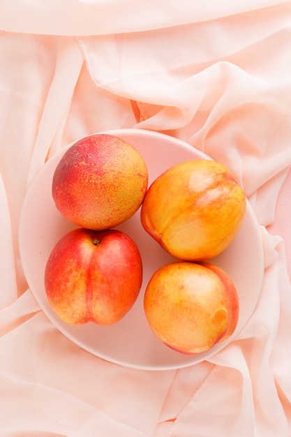 Free photo fresh nectarines in a plate on pink textile surface, high angle view.