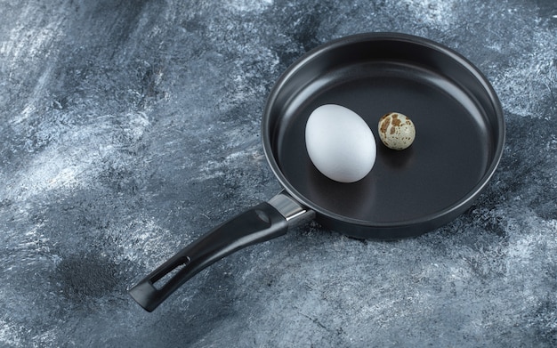 Free Photo fresh organic chicken and quail eggs in black frying pan.