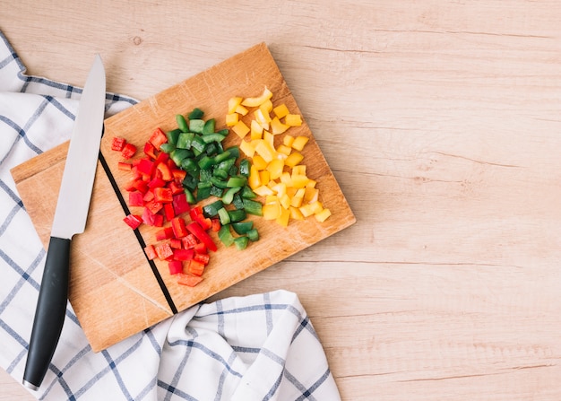 Fresh organic chopped red; yellow and green bell peppers on chopping board with knife over the wooden desk