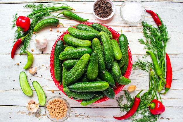 Free Photo fresh organic cucumbers in red basket on white wooden table with green and red and chili peppers, fennel, salt, black peppercorns, garlic, pea, close up, healthy concept, top view, flat lay