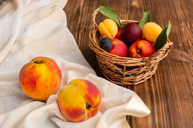 Free photo fresh peaches along with basket full of apricots and plums on wood