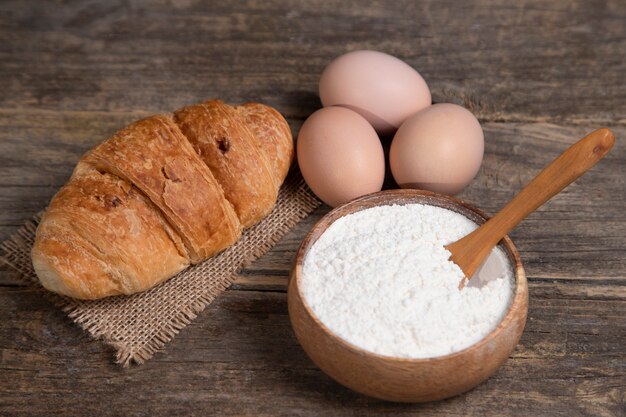 Fresh plain croissants, flour and raw eggs on wooden surface. High quality photo