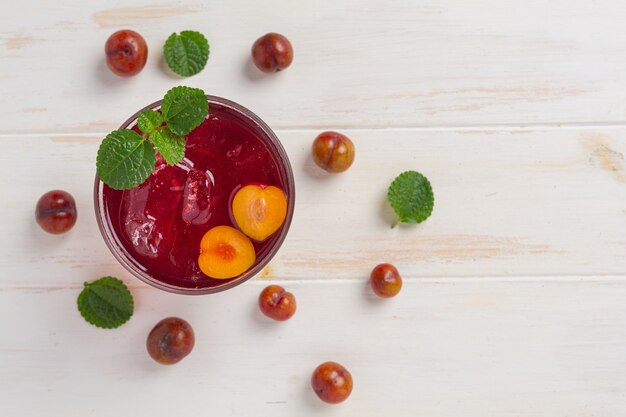 Fresh plums juice on the white wooden surface.