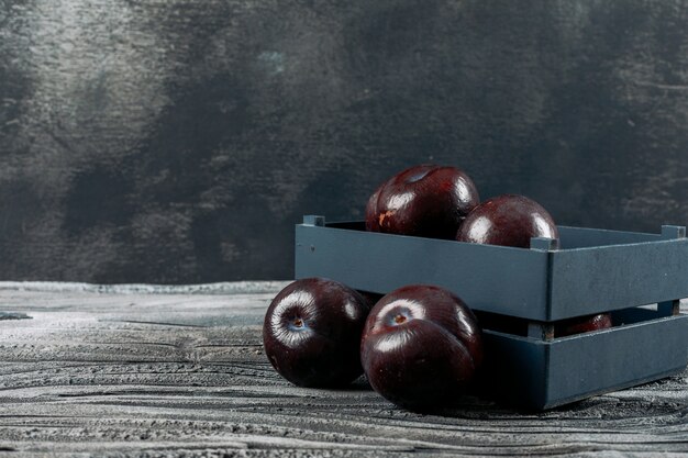 Fresh plums in a plate on a dark grey background. side view.