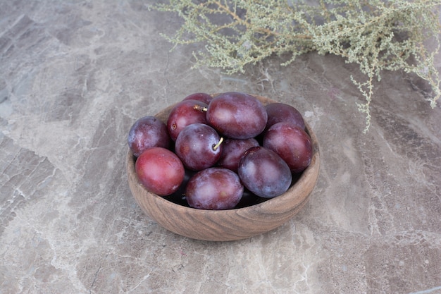 Fresh plums in wooden bowl on stone background. 