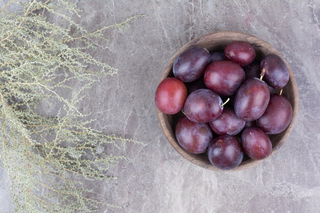 Fresh plums in wooden bowl on stone background. 