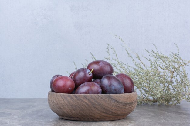 Fresh plums in wooden bowl on stone table. 