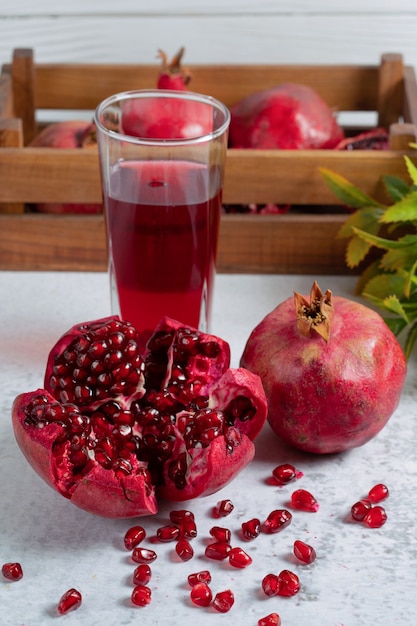 Fresh pomegranate sliced or whole with glass of juice on grey wall.