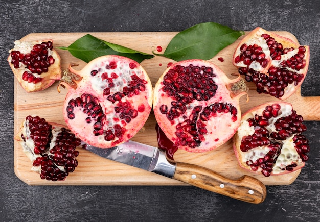 fresh pomegranates with knife top view on wooden cutting board on dark