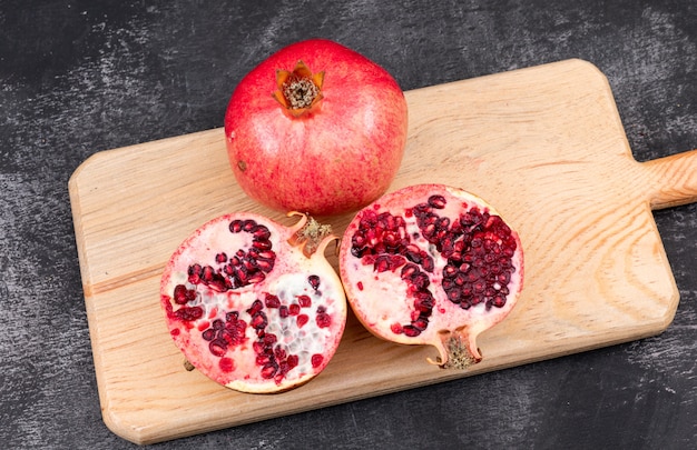 fresh pomegranates on wooden cutting board on dark