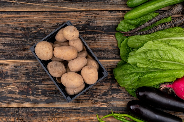 Fresh potato in black basket, with vegetables on wooden table