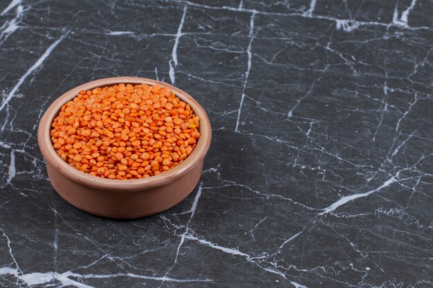 Fresh raw Lentils in pottery bowl over black stone.