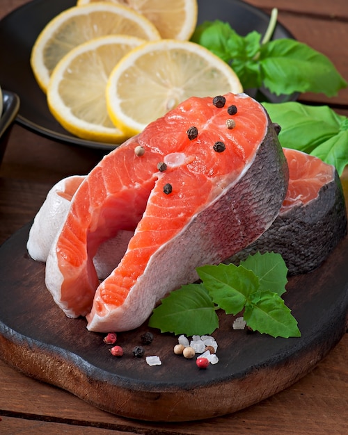 Fresh and raw steaks trout on a wooden cutting board with sliced lemon, rosemary and pepper