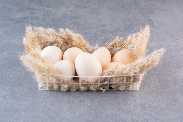 Fresh raw white chicken eggs with wheat ears placed on stone table .