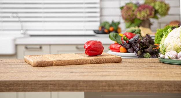 Free photo fresh red bell pepper on a wooden plank against the background of a kitchen interior.