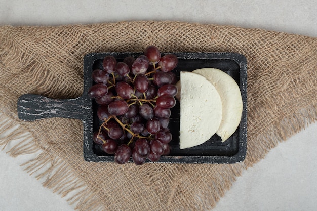 Fresh red grapes and white cheese on black board