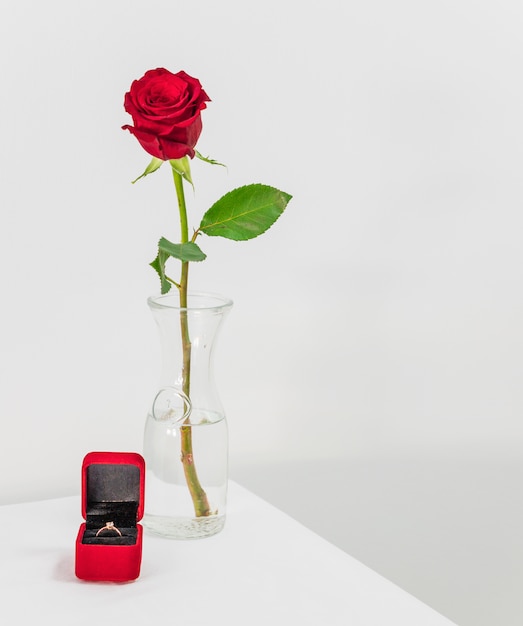 Fresh red rose in vase and present box with ring on table