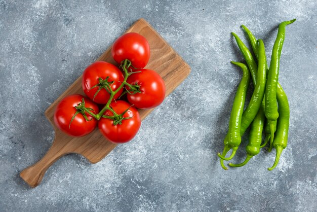 Fresh red tomatoes on wooden board with chili peppers.