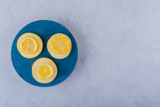 Free photo fresh ripe lemon and apple slices on blue board.