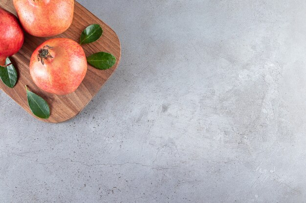 Fresh ripe pomegranates with green leaves on wooden cutting board. 