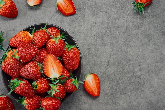 Fresh ripe strawberries and half a berry in a plate on a gray table top view with copy space Seasonal juicy berry