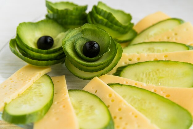 Fresh slices of cheese, cucumber and avocado with olives on dish