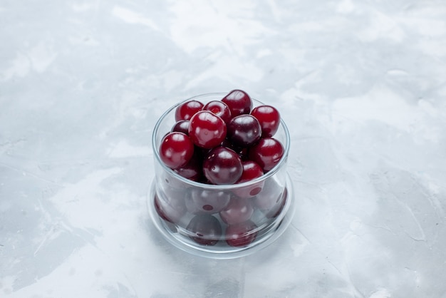 fresh sour cherries inside little glass cup on light-white desk