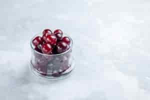 Free photo fresh sour cherries inside little glass cup on white-light desk, fruit sour vitamine photo