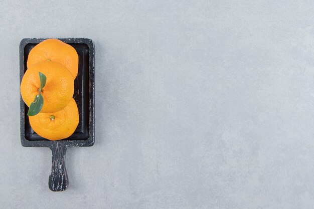 Fresh tangerines with leaves on black cutting board. 