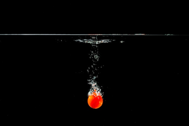 Fresh tomato falling in clear water against black background