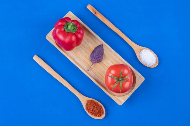 Fresh tomato, garlic and red bell pepper on wooden plate with spices.