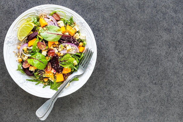 Fresh vegetable salad with beetroot arugula red onion sorrel chickpeas pumpkin and grapes in a white plate on a black background Top view