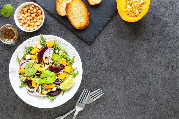 Fresh vegetable salad with beets, arugula, red onion and sorrel in a white plate with pumpkin, toasts and chickpeas