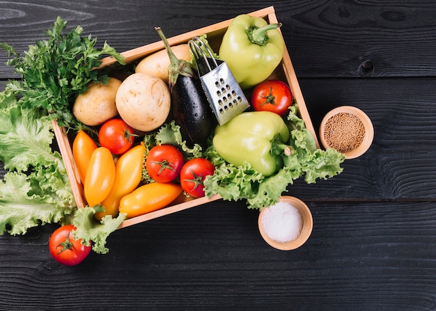 Free photo fresh vegetables in container and spices on black wooden background