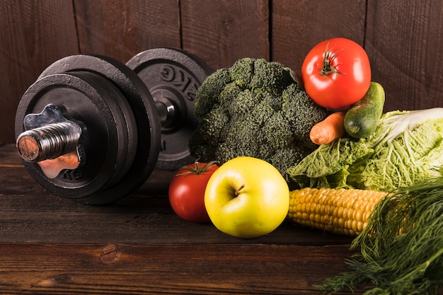 Fresh vegetables and dumbbells on wooden background