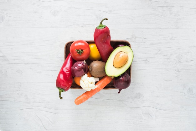 Free photo fresh vegetables and fruits in container on white wooden backdrop