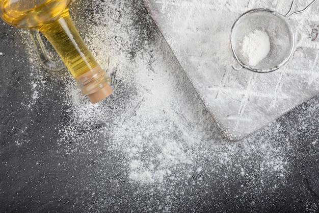 Fresh wheat floor spilled on wooden board with glass of oil